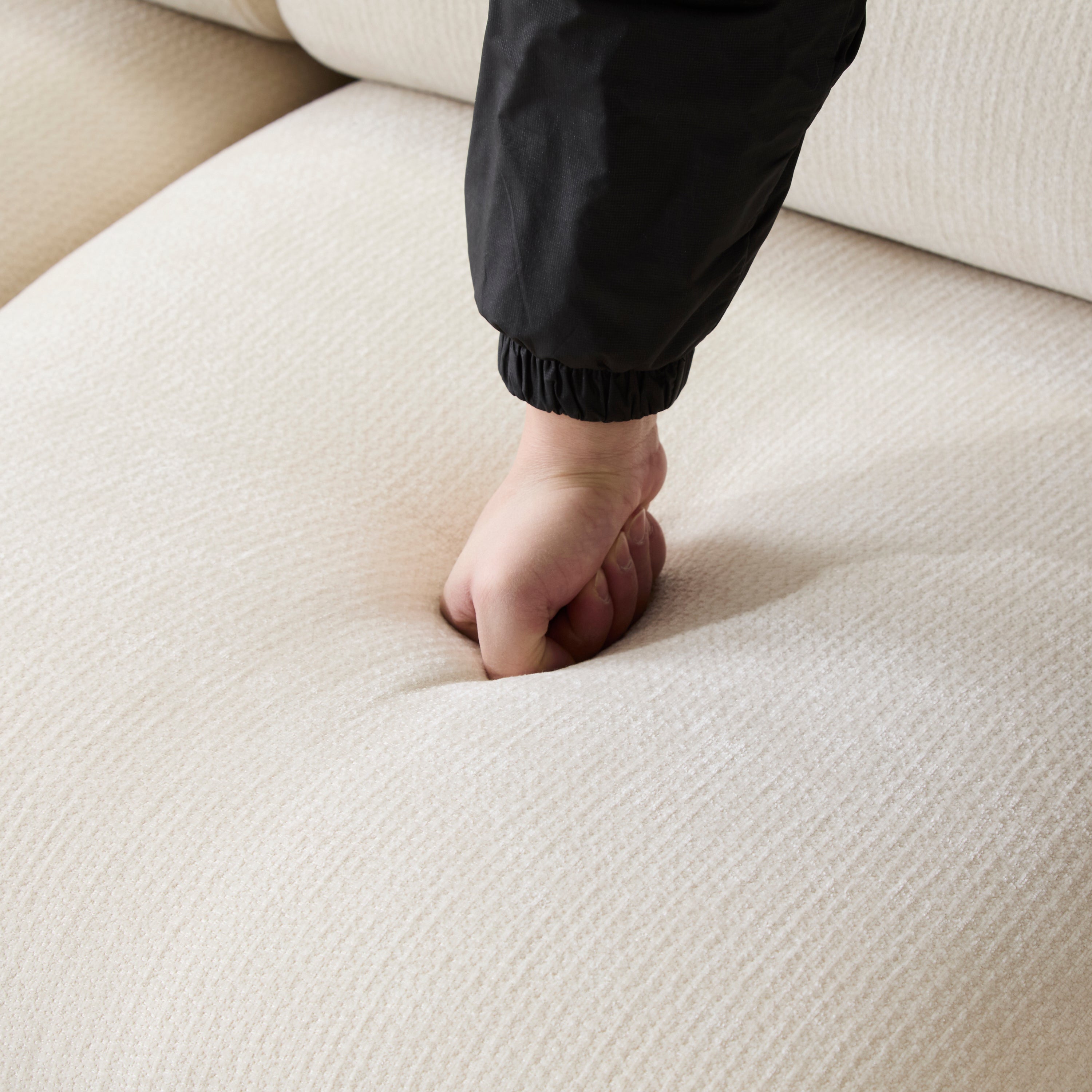 Hand pressing into the seat cushion of the Evelyn modular L shaped chenille sofa, showing its soft and resilient padding.