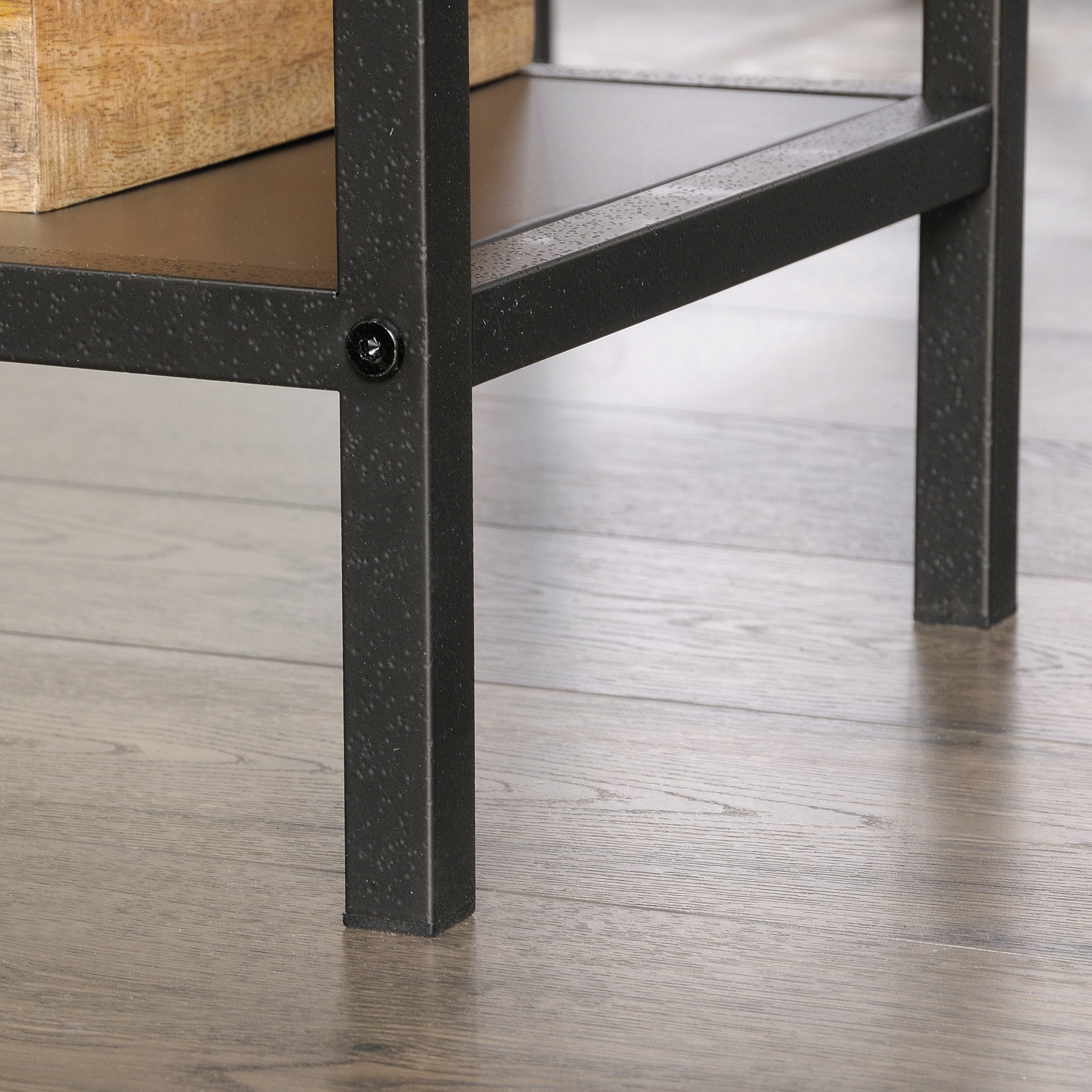 Detail of textured black metal leg on L-shaped computer desk, brown finish, highlighting industrial style and sturdy frame design.