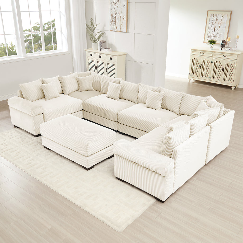 Oversized cream corduroy modular sectional sofa with wide armrests and a matching ottoman in a bright living room.