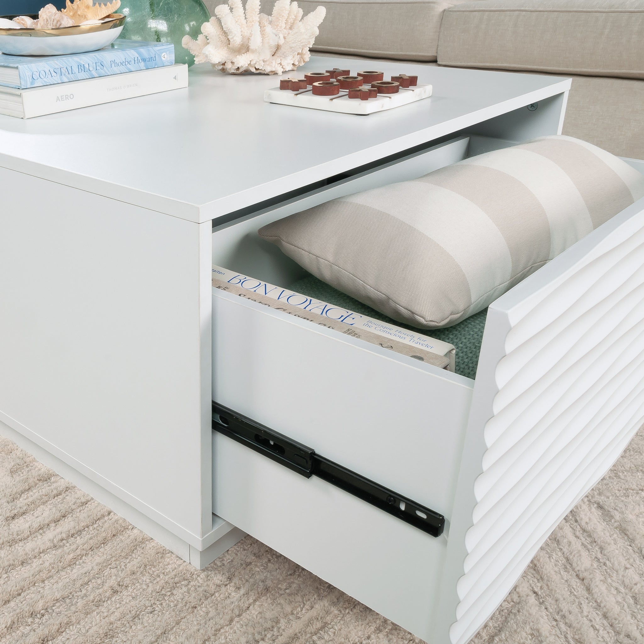 Open drawer of the white coffee table revealing spacious storage with books and a pillow, perfect for organizing living room essentials.