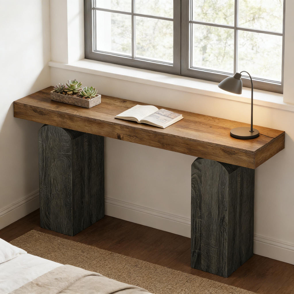 Contemporary console table with a thick wood top and arched, dark charcoal-textured pillar bases by a window.