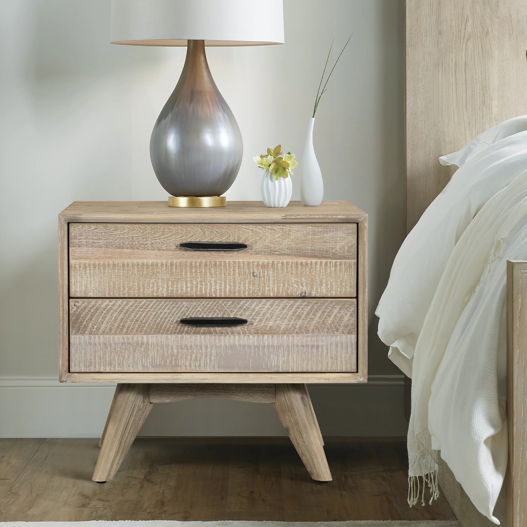 Mid-century modern gray acacia wood nightstand with two drawers, black hardware, and angled legs next to a bed.