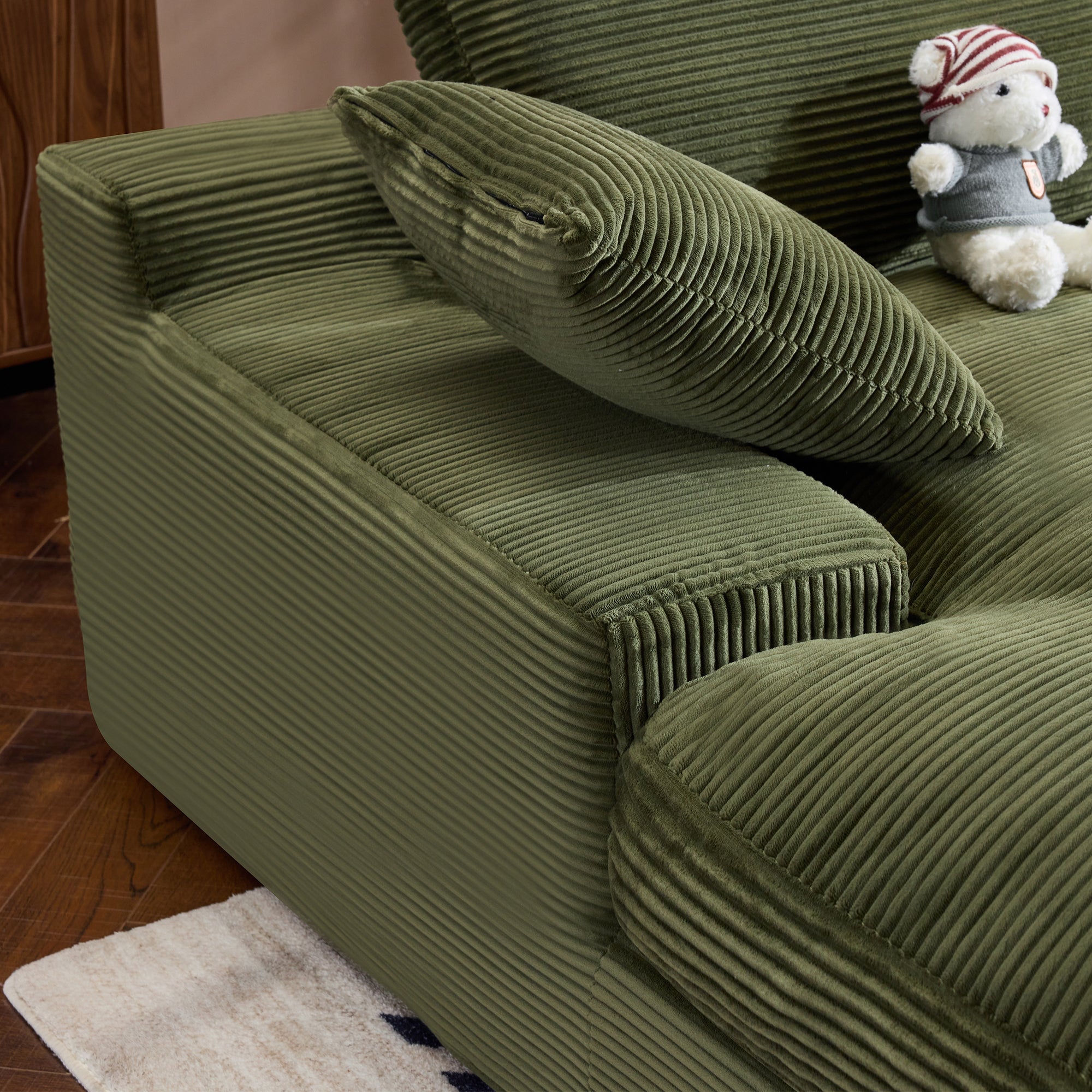 Detailed view of green corduroy sofa armrest and cushion. Ribbed texture and foam filler offer stylish comfort.