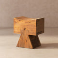 Sculptural ottoman in honey-toned reclaimed pine wood with a curved seat and a sturdy, geometric pedestal base.