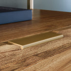 Close-up of gold drawer handle on brown lateral file cabinet, featuring minimalist hardware for a clean, modern look.