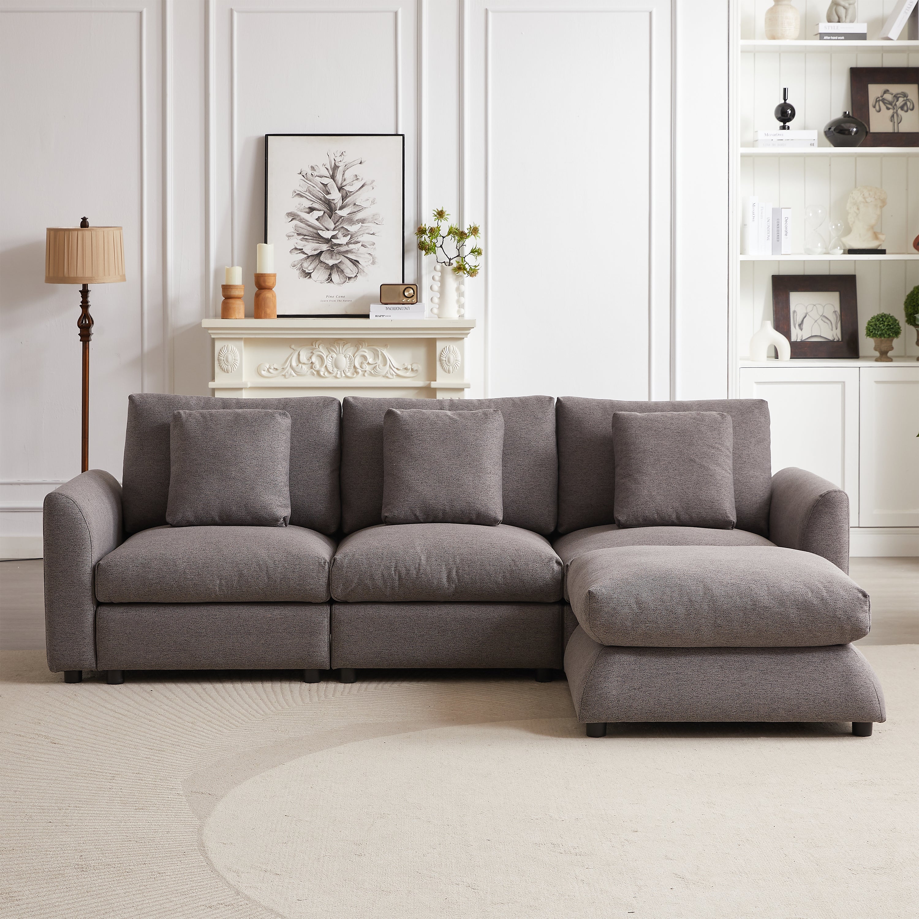 Front view of gray upholstered modular sofa with ottoman, featuring three seats and five matching pillows in a stylish living room.