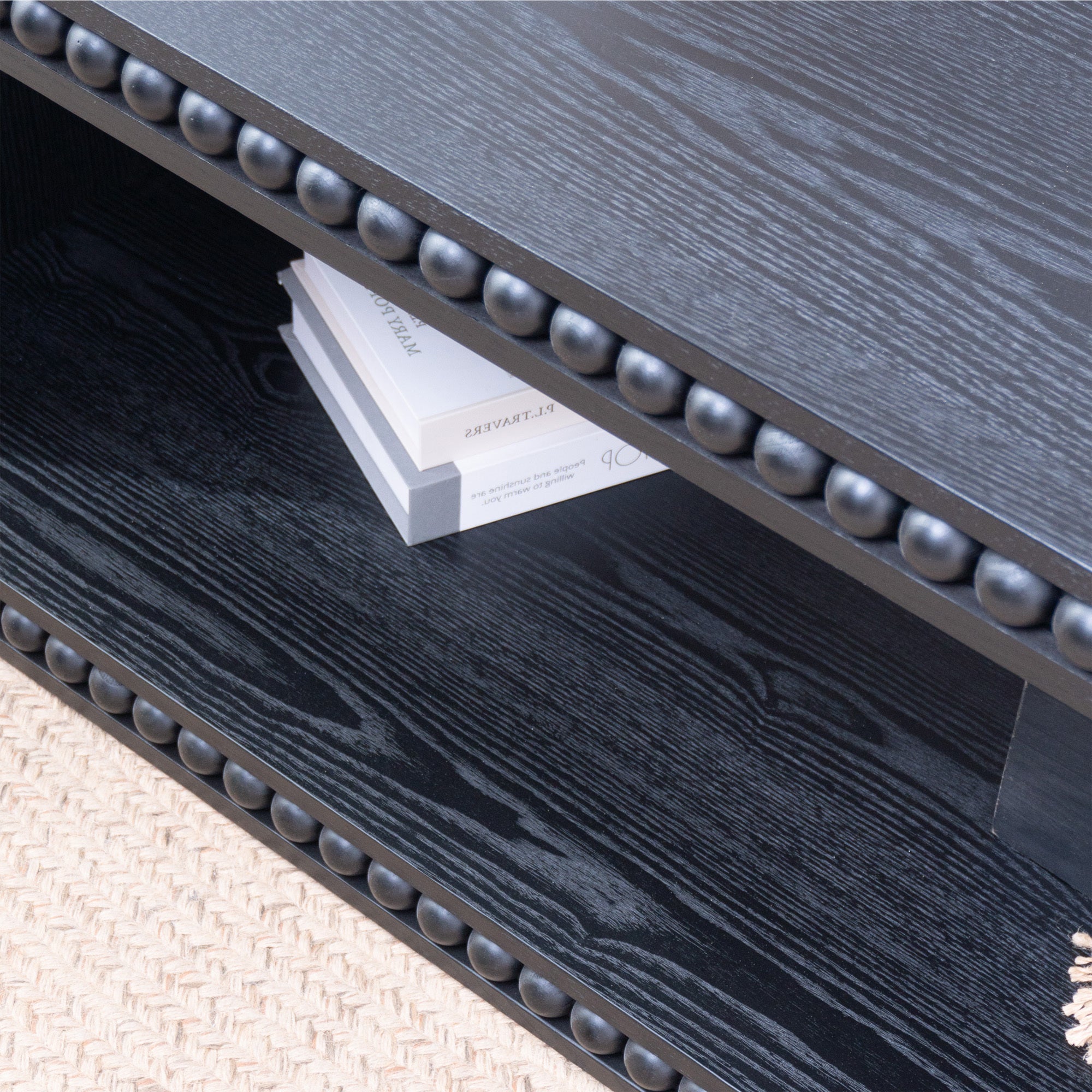 Detail of Black Beaded Coffee Table’s open shelf with books and beaded trim, emphasizing storage and decorative features.