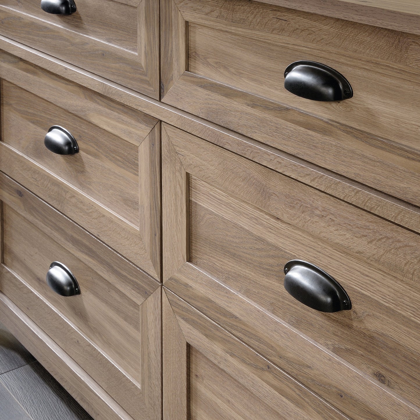 Close-up of the brown dresser's drawer fronts showing detailed wood grain texture and black cup-style handles in a transitional design.