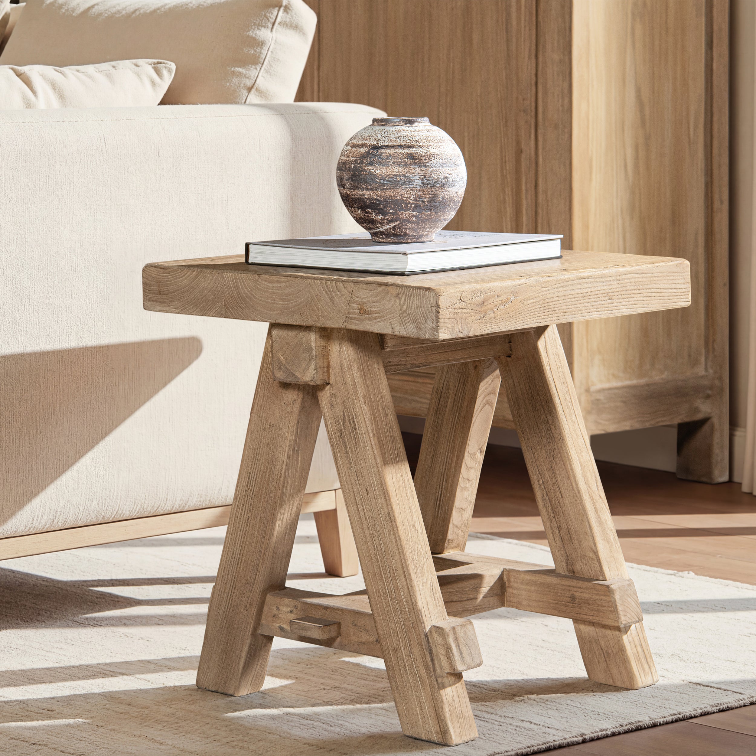 Square light brown reclaimed elm wood trestle side table with a rustic, sturdy design on a neutral area rug.