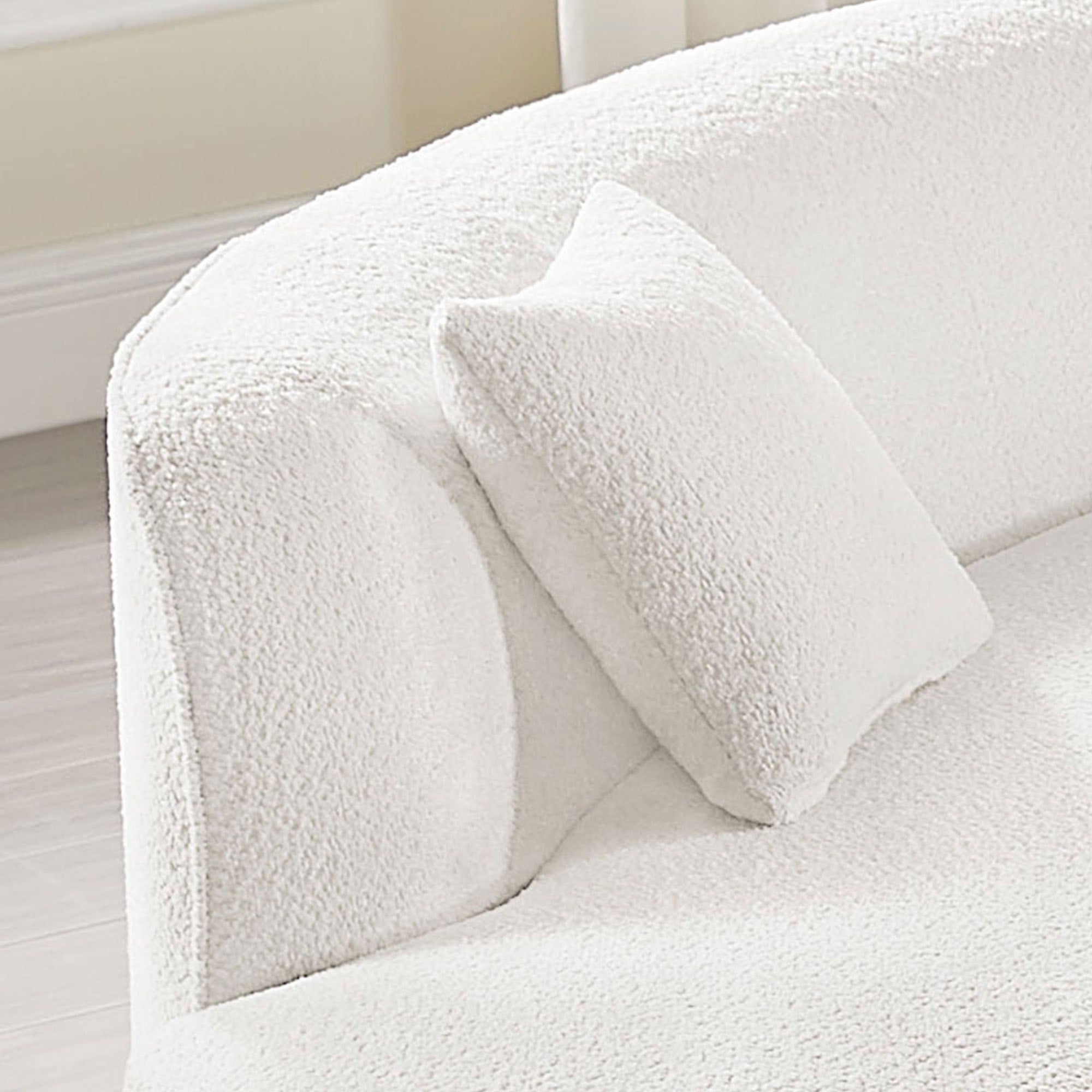 Detail of armrest and cushion on modern curved sofa set in white bouclé, showcasing cozy texture and refined craftsmanship.