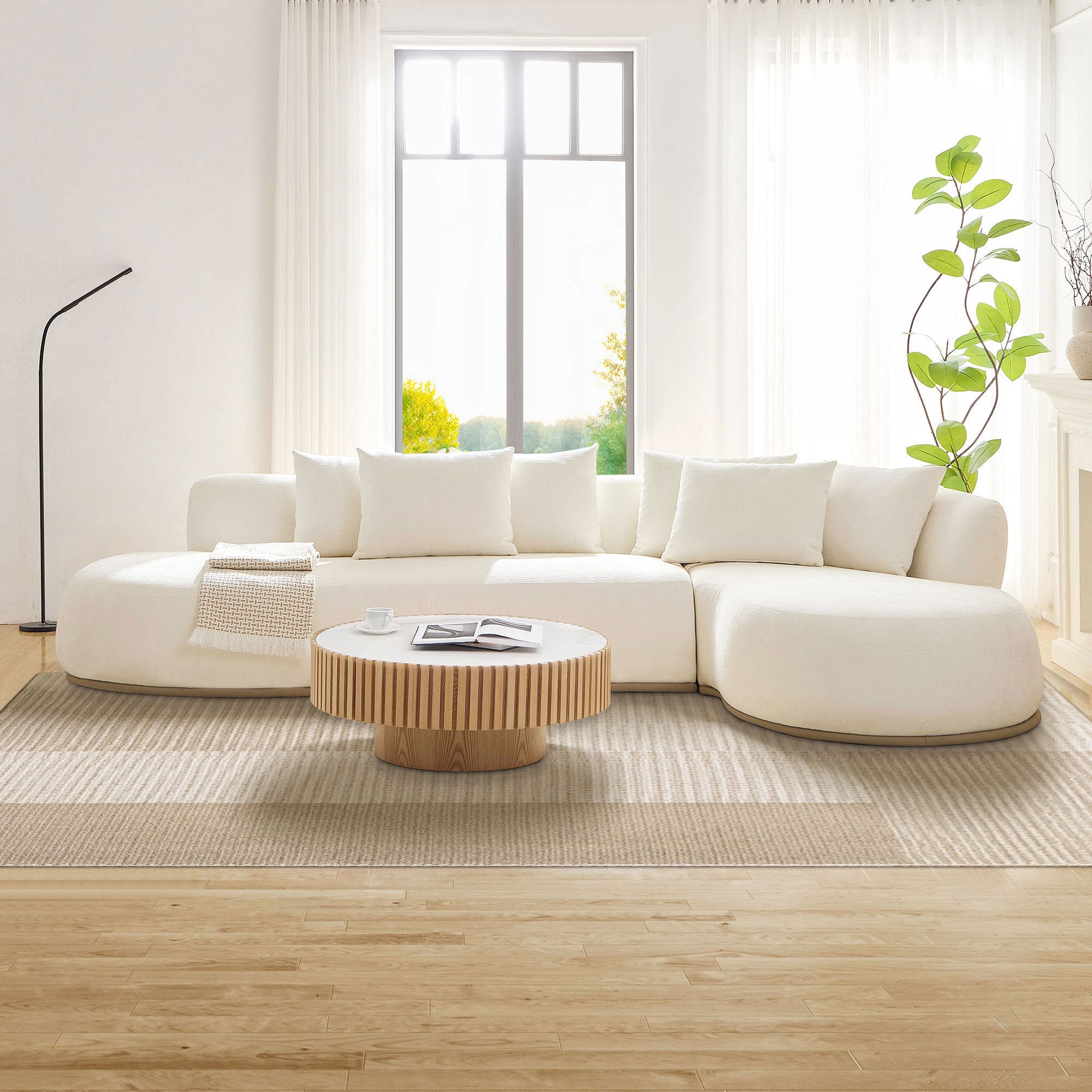 Beige oversized L-shape sectional sofa with right chaise, styled with a round wood coffee table and neutral rug in a sunlit living space.