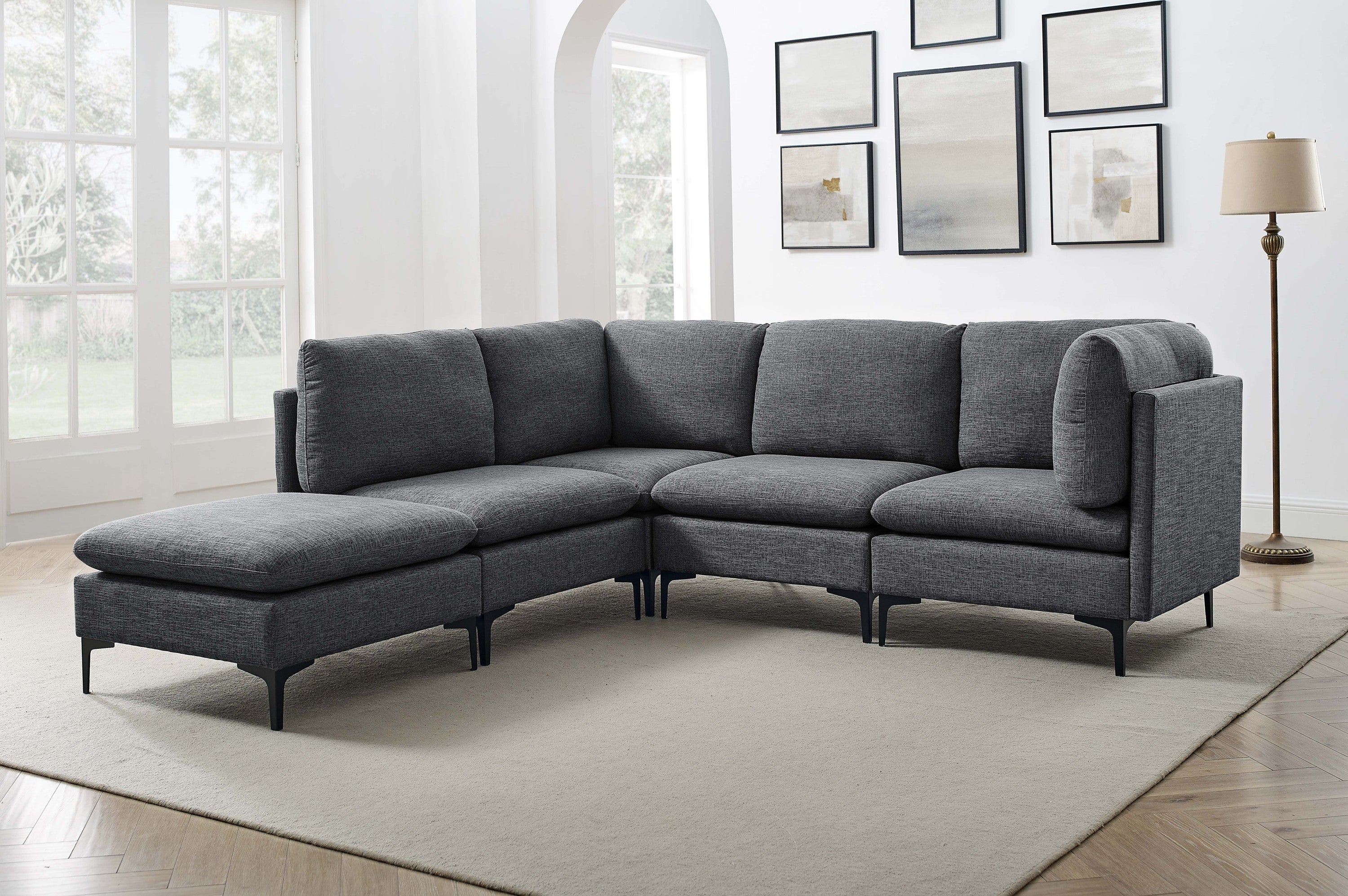 Modern charcoal grey linen modular sectional sofa with plush cushions and slim black metal legs in a bright living room.