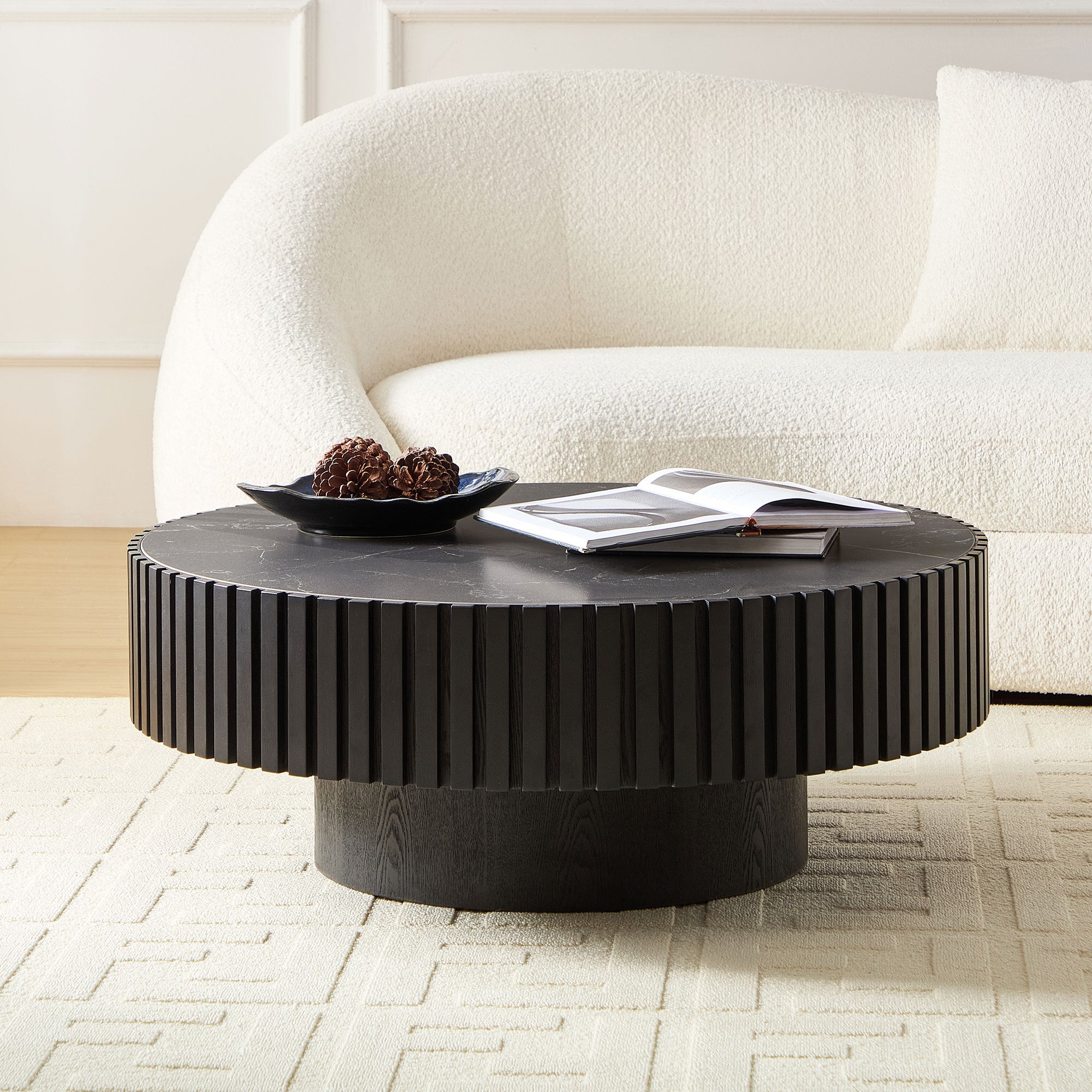 Contemporary round coffee table with black sintered stone top and fluted base, styled in a modern living room with neutral tones.