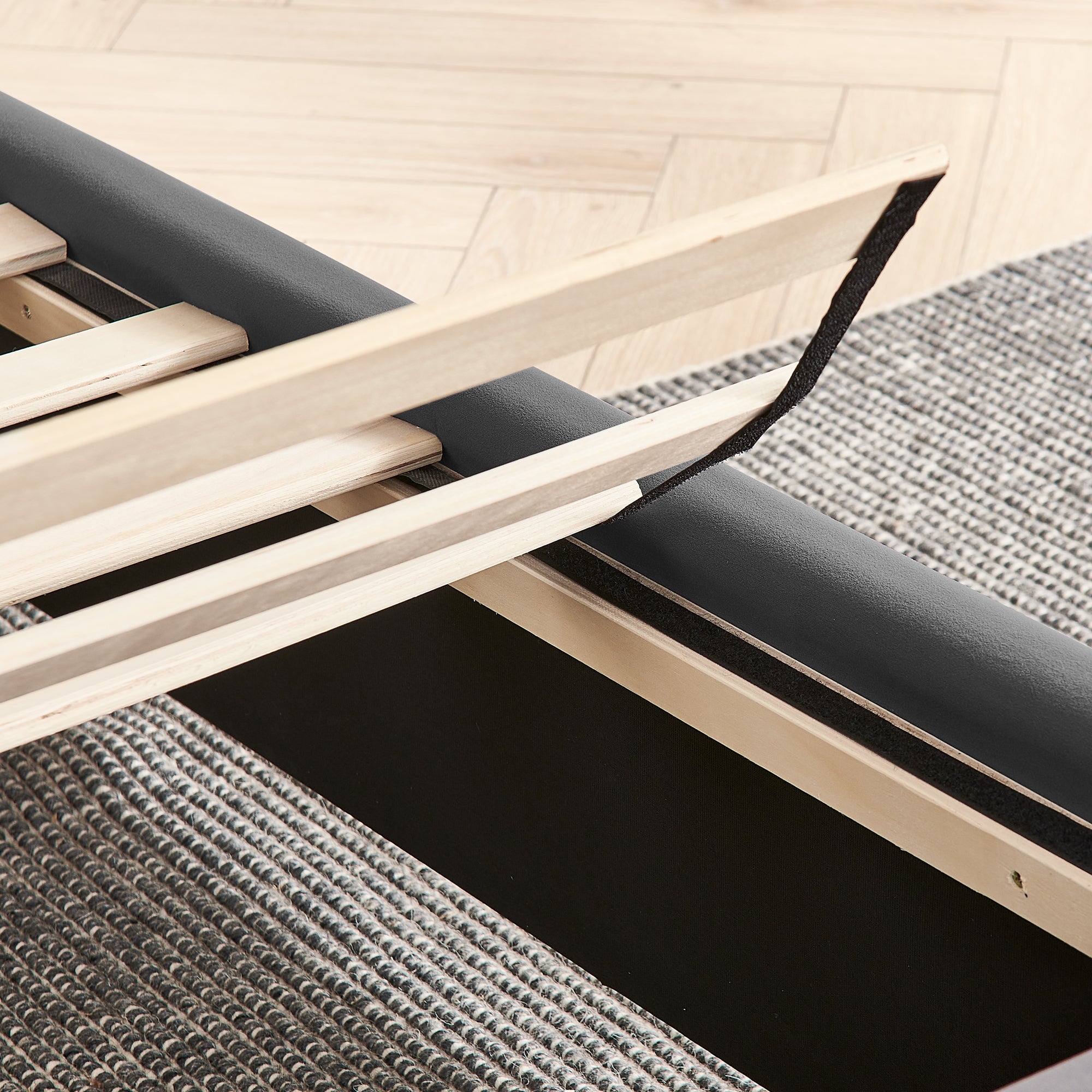 Detail of wooden slat support system on upholstered queen bed frame, showing easy assembly and no box spring requirement.