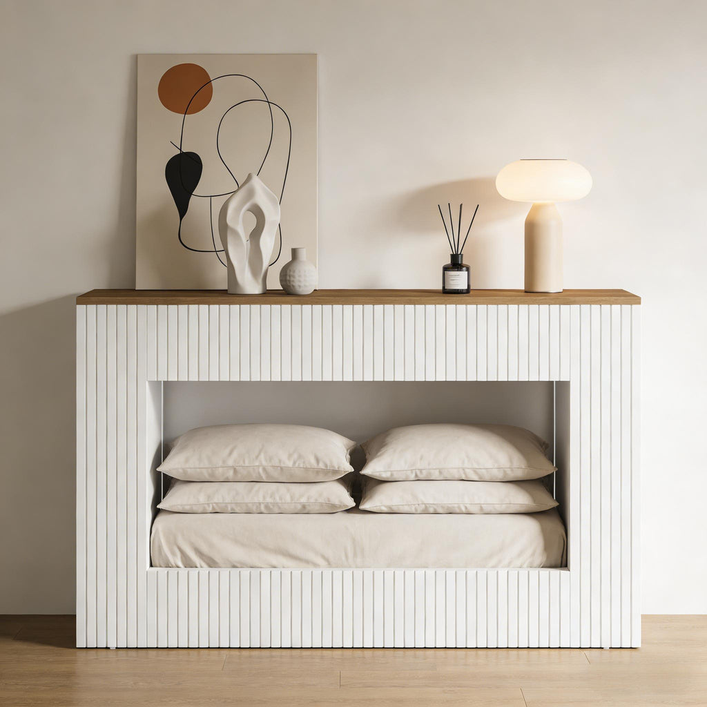 Modern white fluted console table with a wooden top, featuring a hollow base area storing beige bedding and pillows.