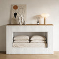 Modern white fluted console table with a wooden top, featuring a hollow base area storing beige bedding and pillows.