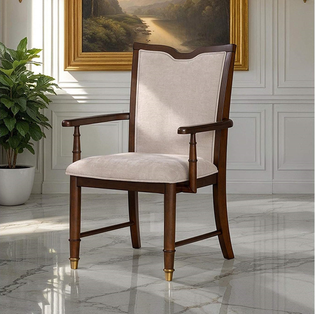 Transitional dining arm chair with beige upholstery, dark cherry wood frame, and gold capped legs in elegant room setting.