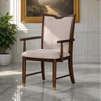 Transitional dining arm chair with beige upholstery, dark cherry wood frame, and gold capped legs in elegant room setting.