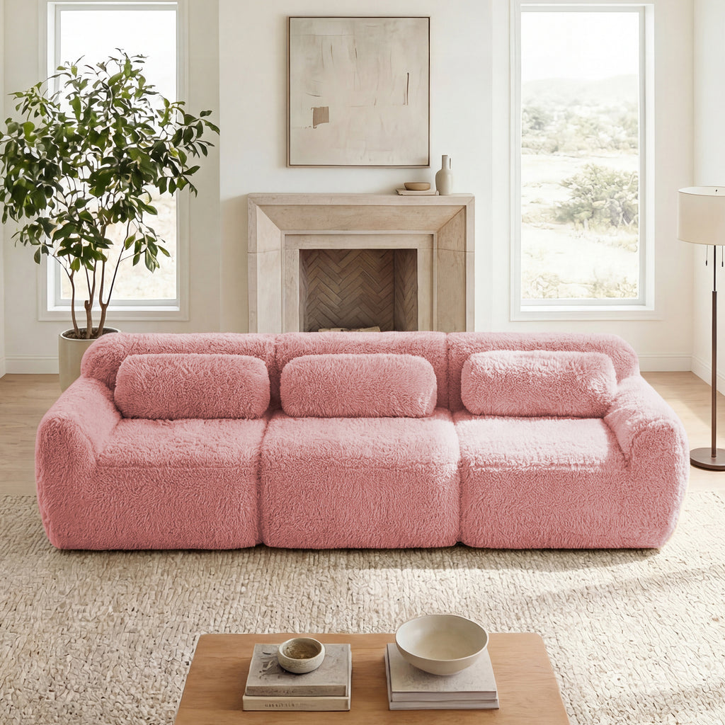 Plush pink modular sectional sofa with fuzzy fabric and three bolster pillows in a cozy, bright living room.