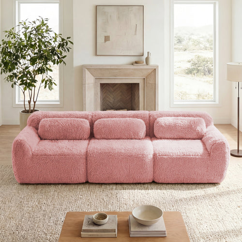 Plush pink modular sectional sofa with fuzzy fabric and three bolster pillows in a cozy, bright living room.