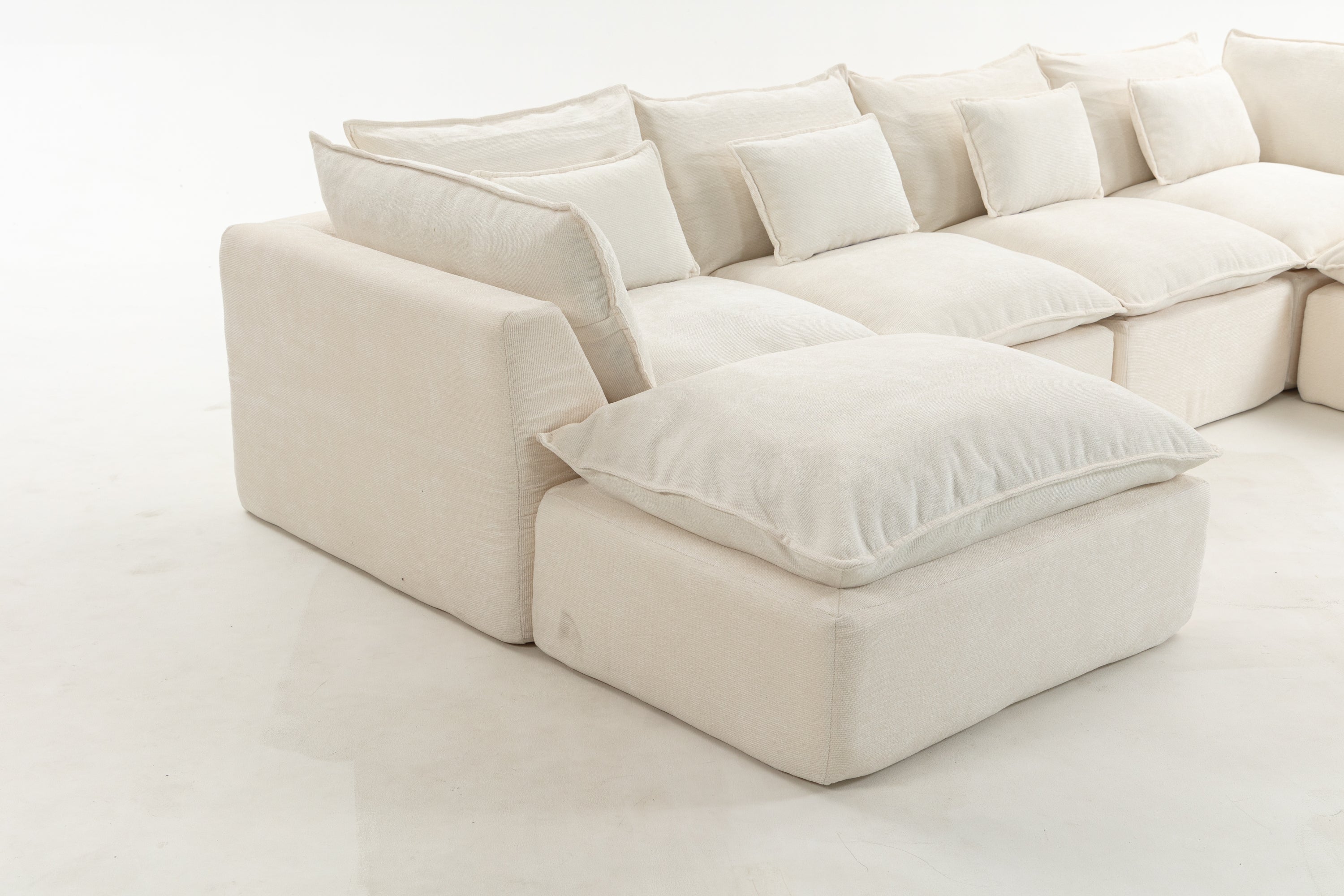 Close-up of left corner of oversized modular sectional sofa. Plush cushions and wide armrest highlight cloud couch comfort.