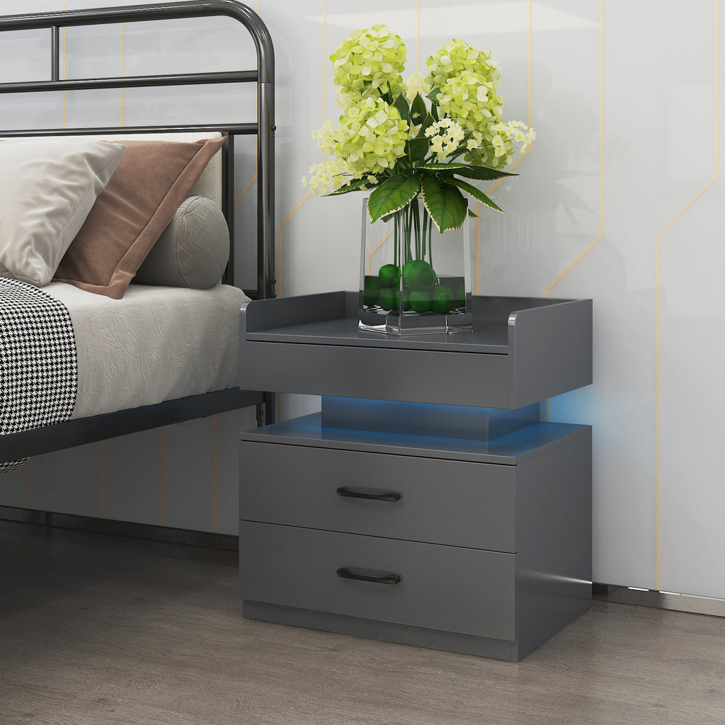 Modern dark gray nightstand with two drawers, black handles, and glowing blue under-shelf LED lighting next to a bed.