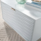 Angled view of the white coffee table with closed drawer, showcasing the ribbed texture and gold-tone handle in a coastal style.