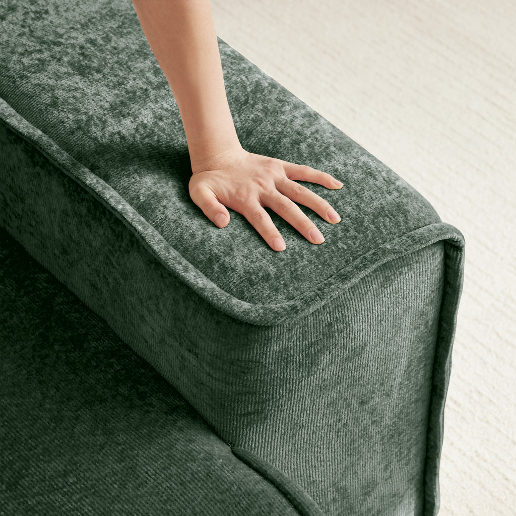 Hand pressing into the cushion of the Modular Green Sofa, demonstrating the softness and plush feel of the velvet upholstery.