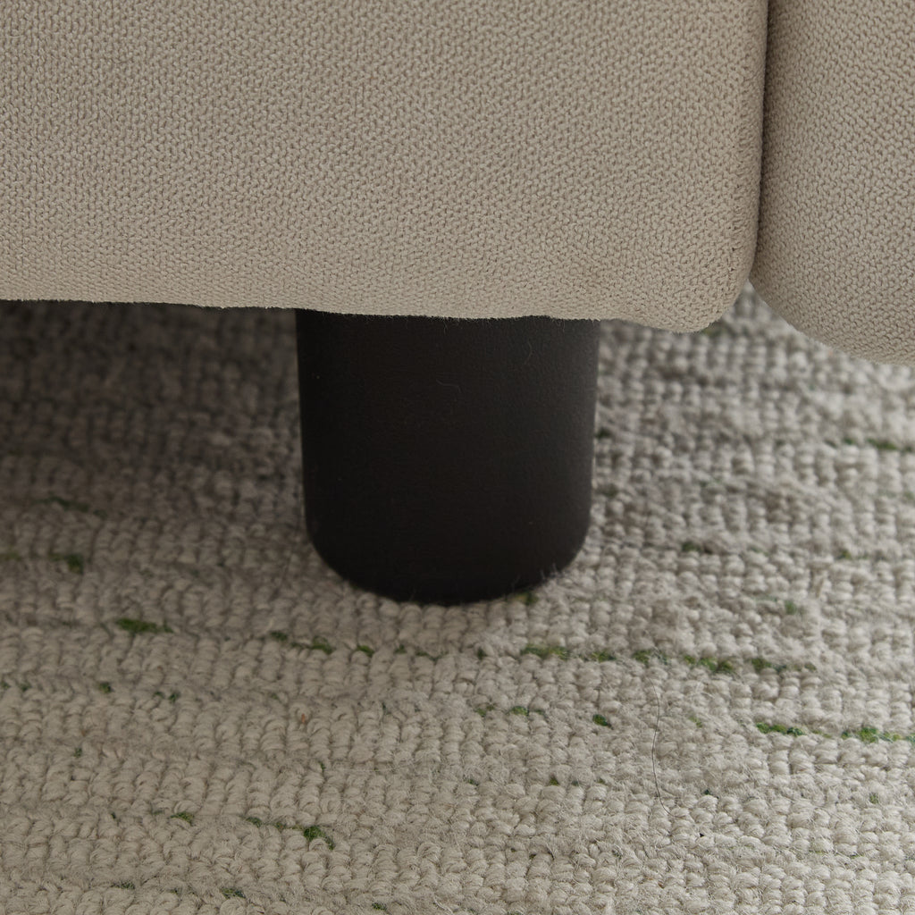 Close-up of black cylindrical leg on the 99 in. 4-piece L shaped modular sectional sofa, resting on a woven area rug.
