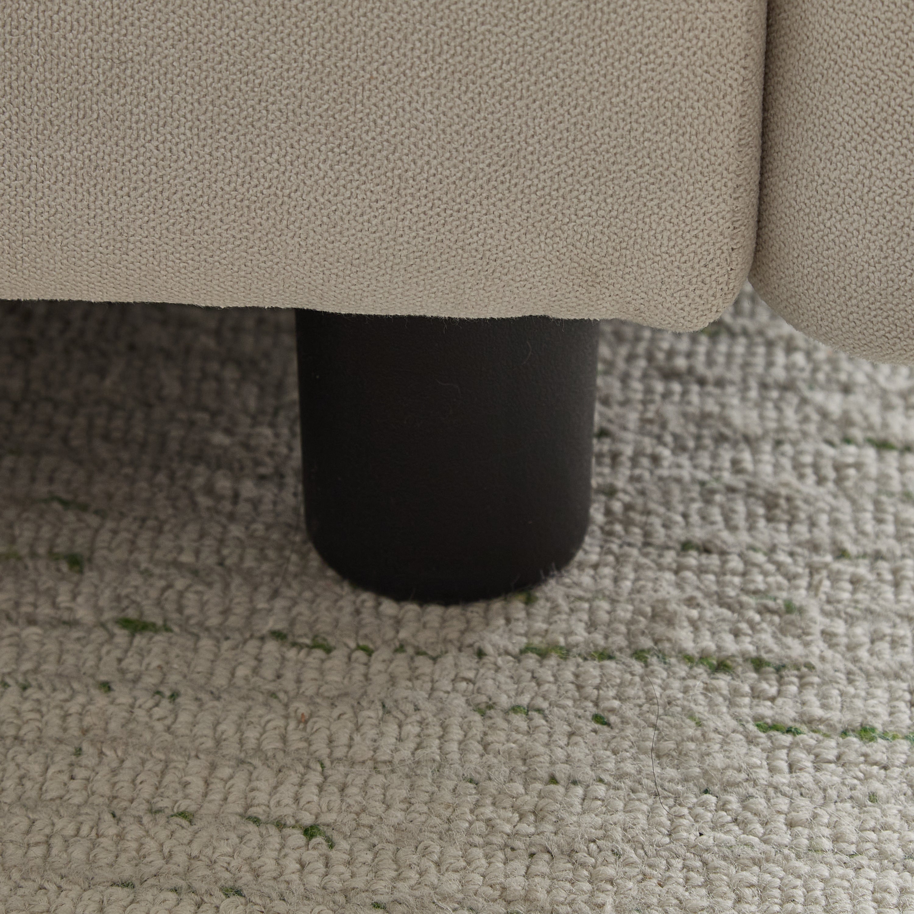 Close-up of black cylindrical leg on the 99 in. 4-piece L shaped modular sectional sofa, resting on a woven area rug.