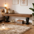 Modern rustic bench with a thick wood-grain top and black curved metal legs, placed in a cozy, styled bedroom setting.