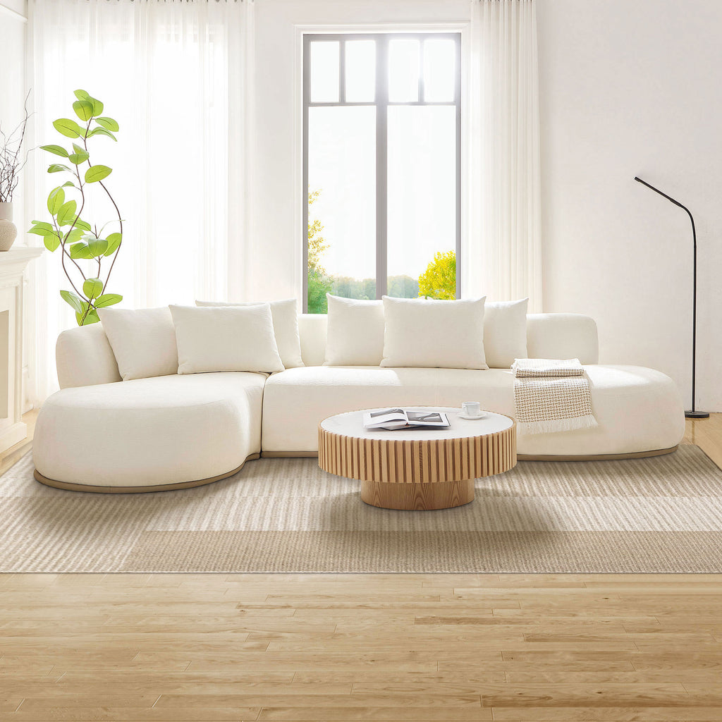 Oversized Beige L-Shape Sectional Sofa with Chaise in bright living room, paired with light wood coffee table and large windows.
