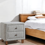 Cleo Gray Boucle Nightstand beside a wooden bed in a modern bedroom. Elegant bedroom furniture with soft boucle texture and wooden legs.