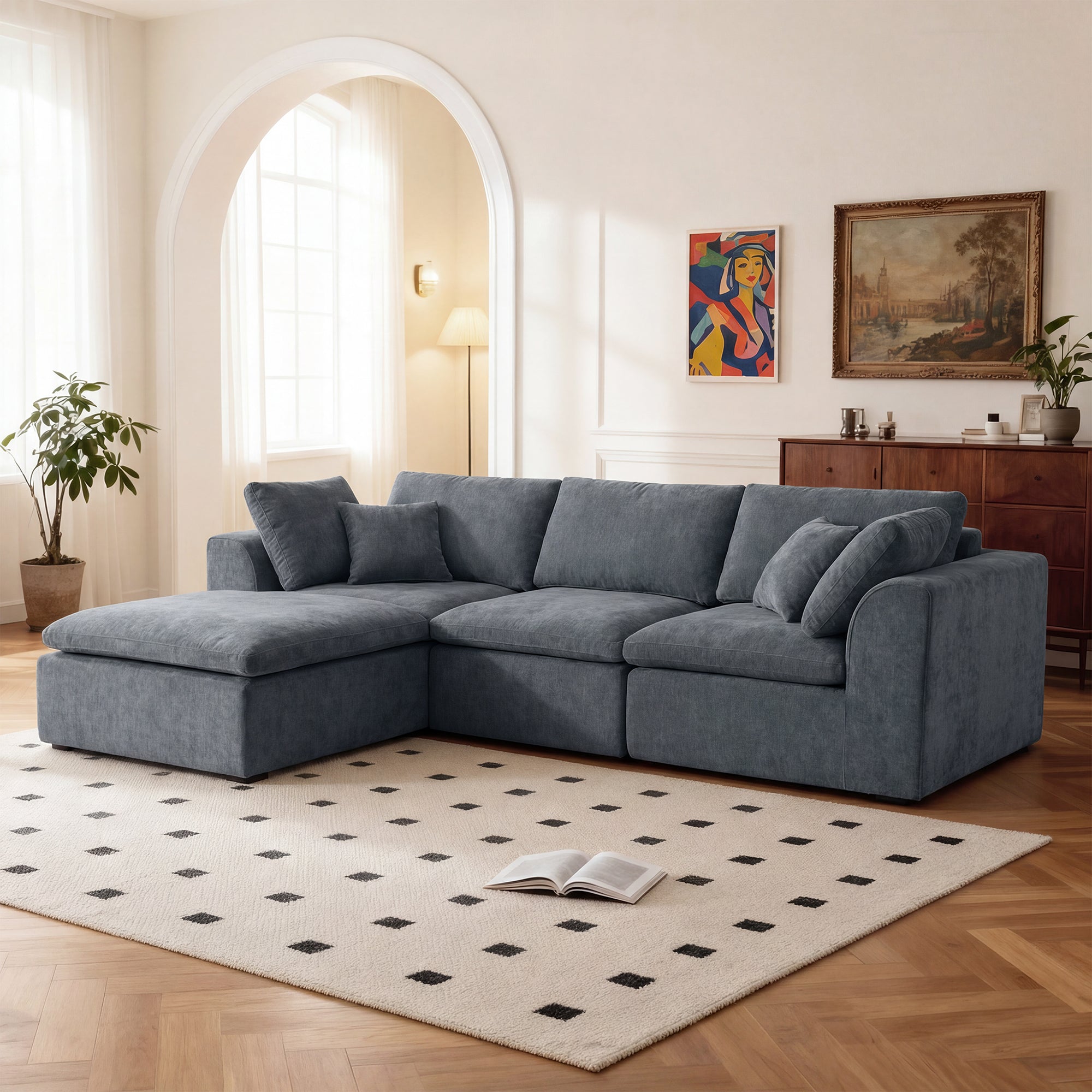 Modern L-shaped sofa with chaise in dark blue chenille fabric, set in a bright living room with wood flooring and minimalist decor.