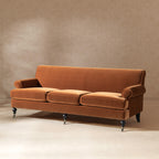 Burnt orange performance velvet three-cushion sofa with a tight back, rolled arms, and turned legs with casters.