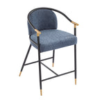 Three-quarter front view of upholstered counter stool with plush blue seat and curved black metal frame accented with gold details.