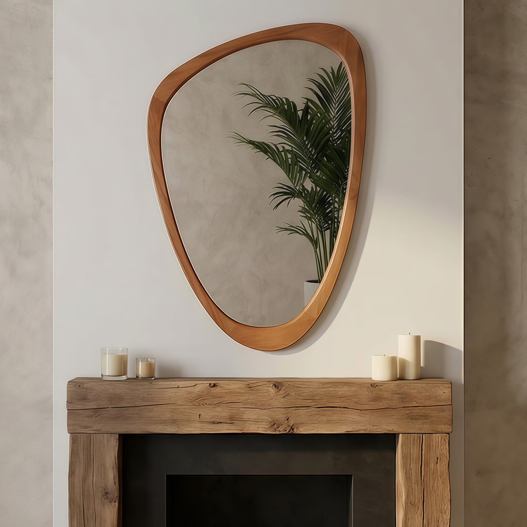 Irregular, pebble-shaped mirror with a smooth, yellowish-brown solid wood frame hanging above a rustic fireplace mantle.