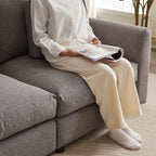 Person sitting on gray modular sofa, reading a magazine, demonstrating the comfort and spacious seating of the upholstered furniture.