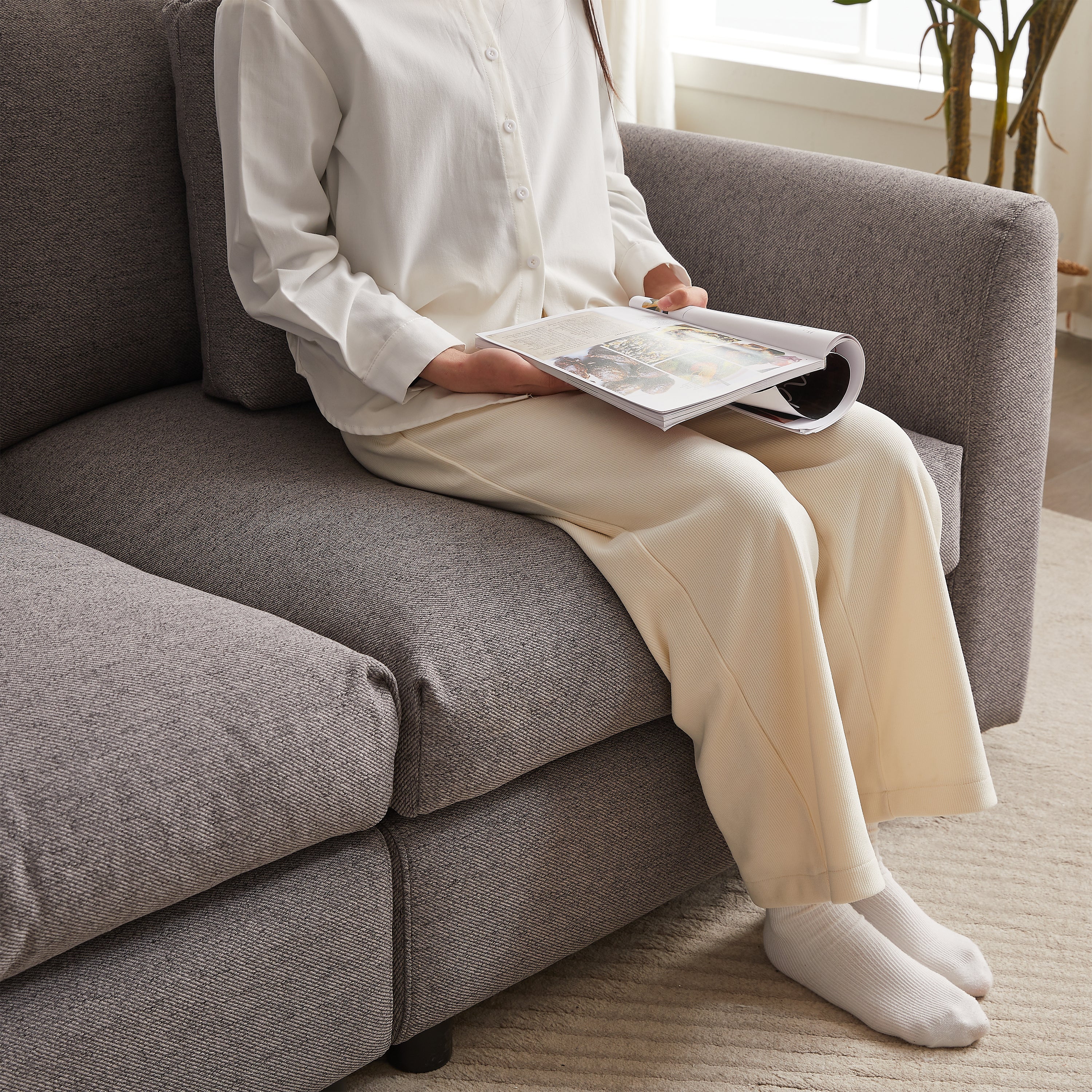 Person sitting on gray modular sofa, reading a magazine, demonstrating the comfort and spacious seating of the upholstered furniture.