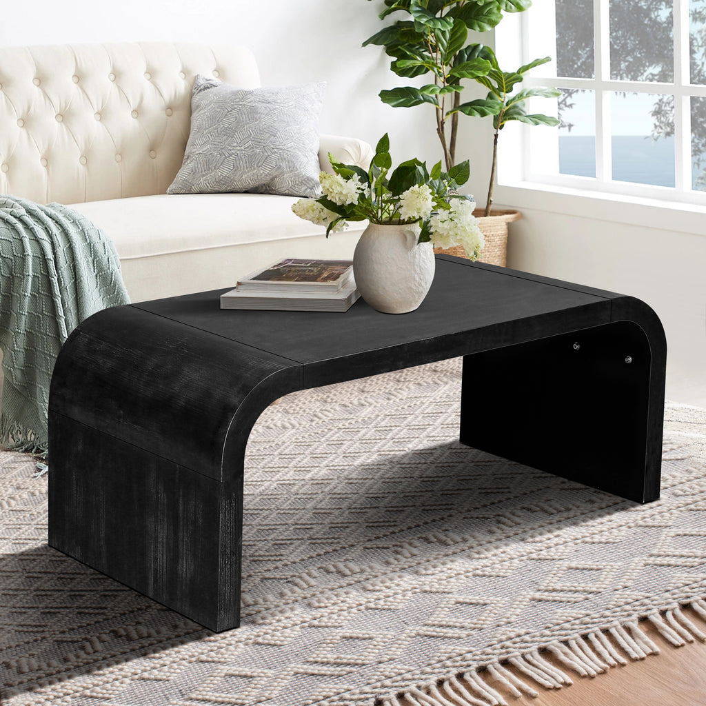 Farmhouse Crafts Coffee Table in black with Art Deco curves, featured in a bright living space with textured rug and cream sofa.