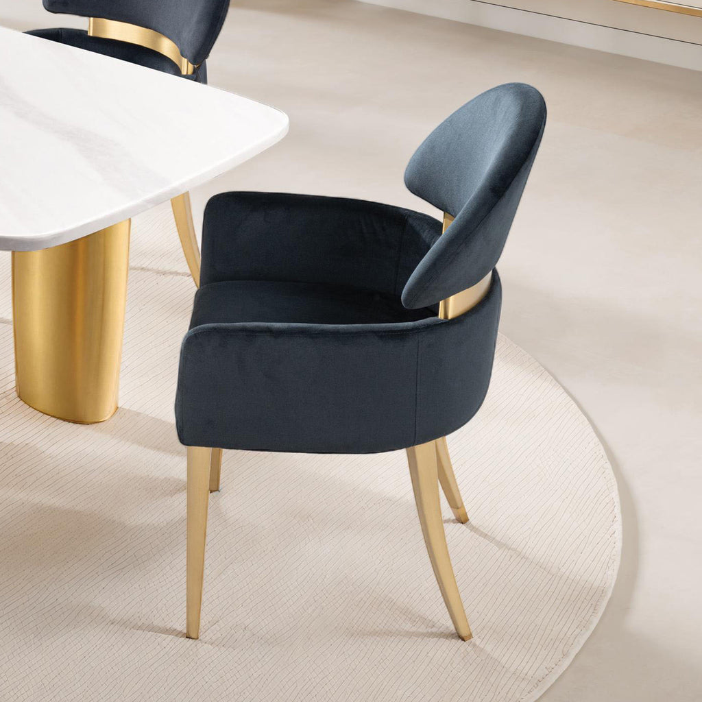 Contemporary black dining arm chair with matte gold stainless steel legs beside a white marble table, perfect for modern interiors.