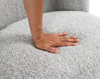 Hand pressing into the cushioned seat of the gray boucle accent chair, demonstrating its plush comfort and quality upholstery.