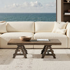 Rectangular coffee table in medium-dark brown reclaimed elm with a rustic trestle base in front of a white sofa.