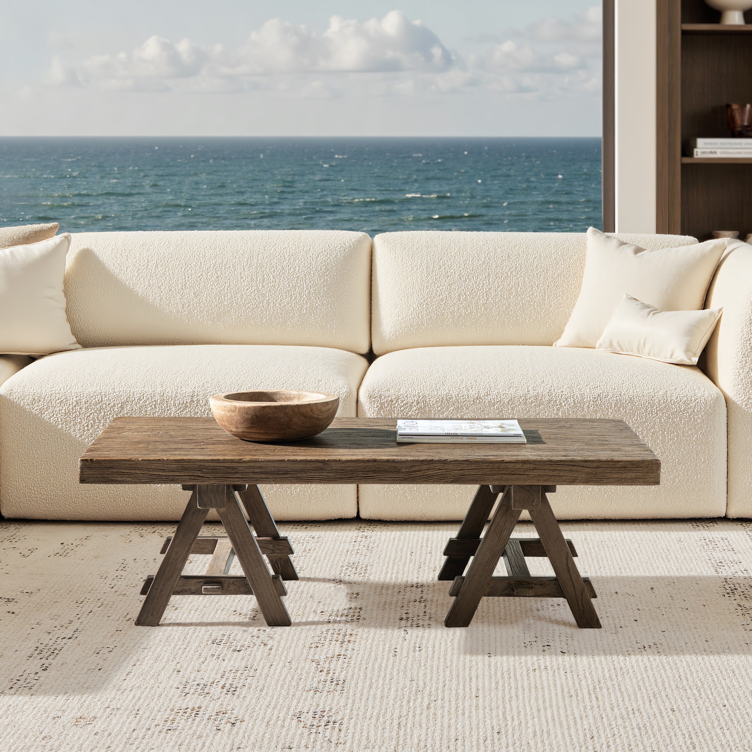 Rectangular coffee table in medium-dark brown reclaimed elm with a rustic trestle base in front of a white sofa.