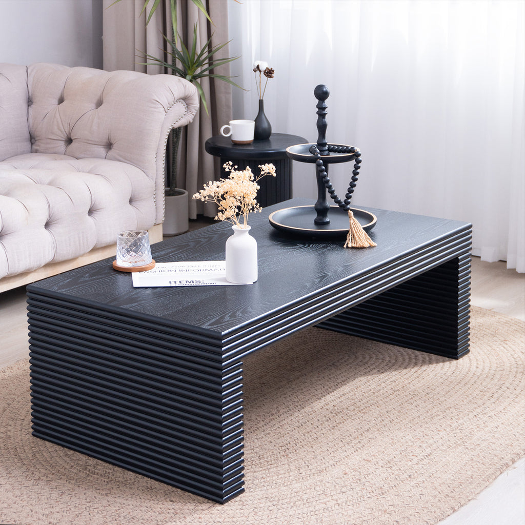 Modern black ribbed coffee table styled in a living room setting, showcasing its sleek rectangular shape and textured finish.