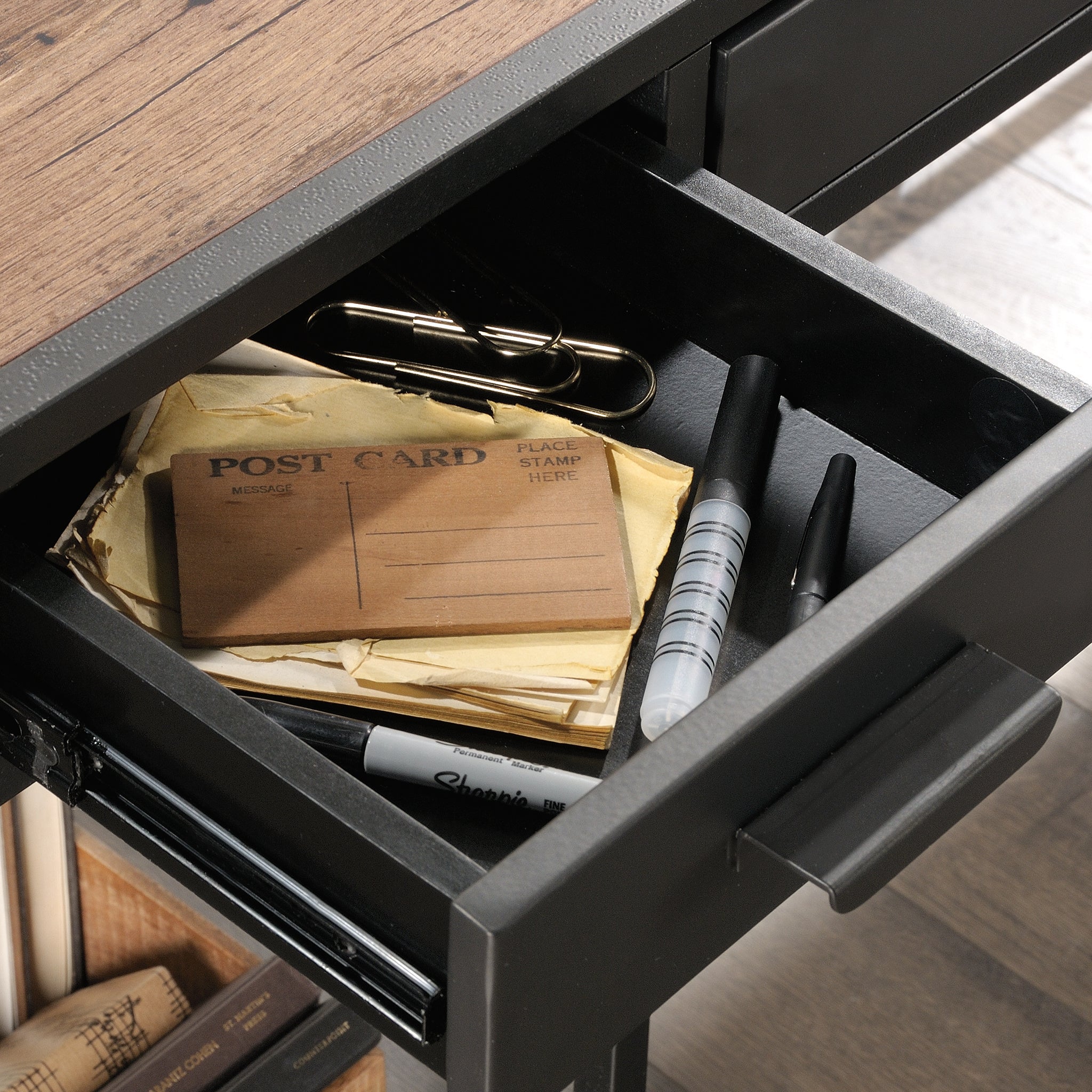 Close-up of small drawer on L-shaped computer desk, brown finish, showing organized office supplies in industrial-style black drawer.