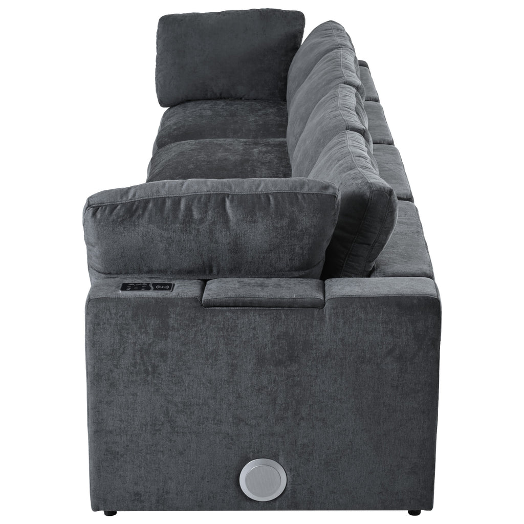 Side view of modular sofa with storage and charging ports, featuring built-in Bluetooth speaker and plush cushions in dark grey fabric.