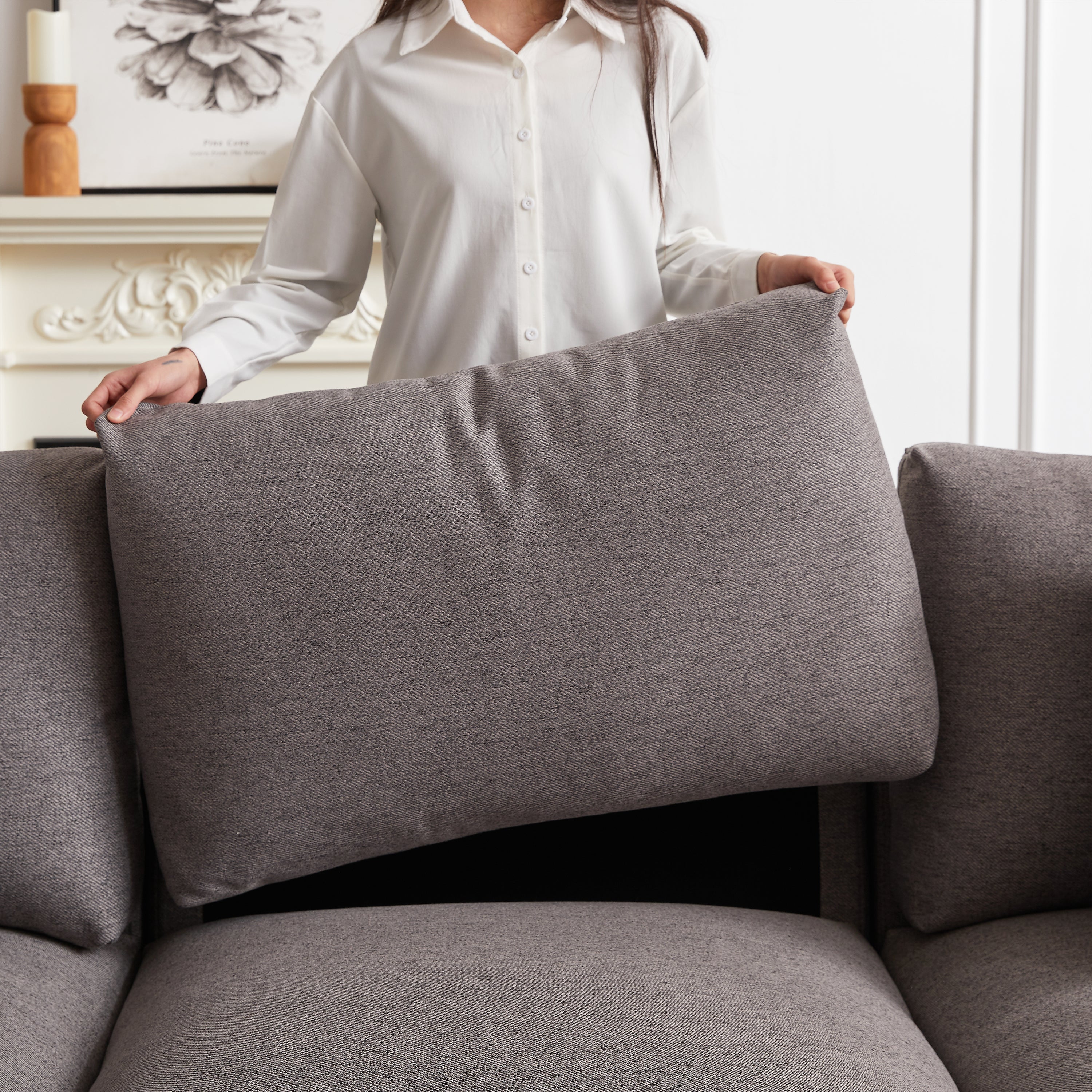 Close-up of person lifting back cushion from modular sofa, showing removable cushions for easy cleaning and maintenance.