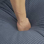 Hand pressing into the soft cushion of the blue corduroy sofa, demonstrating its plush and supportive padding for ultimate relaxation.