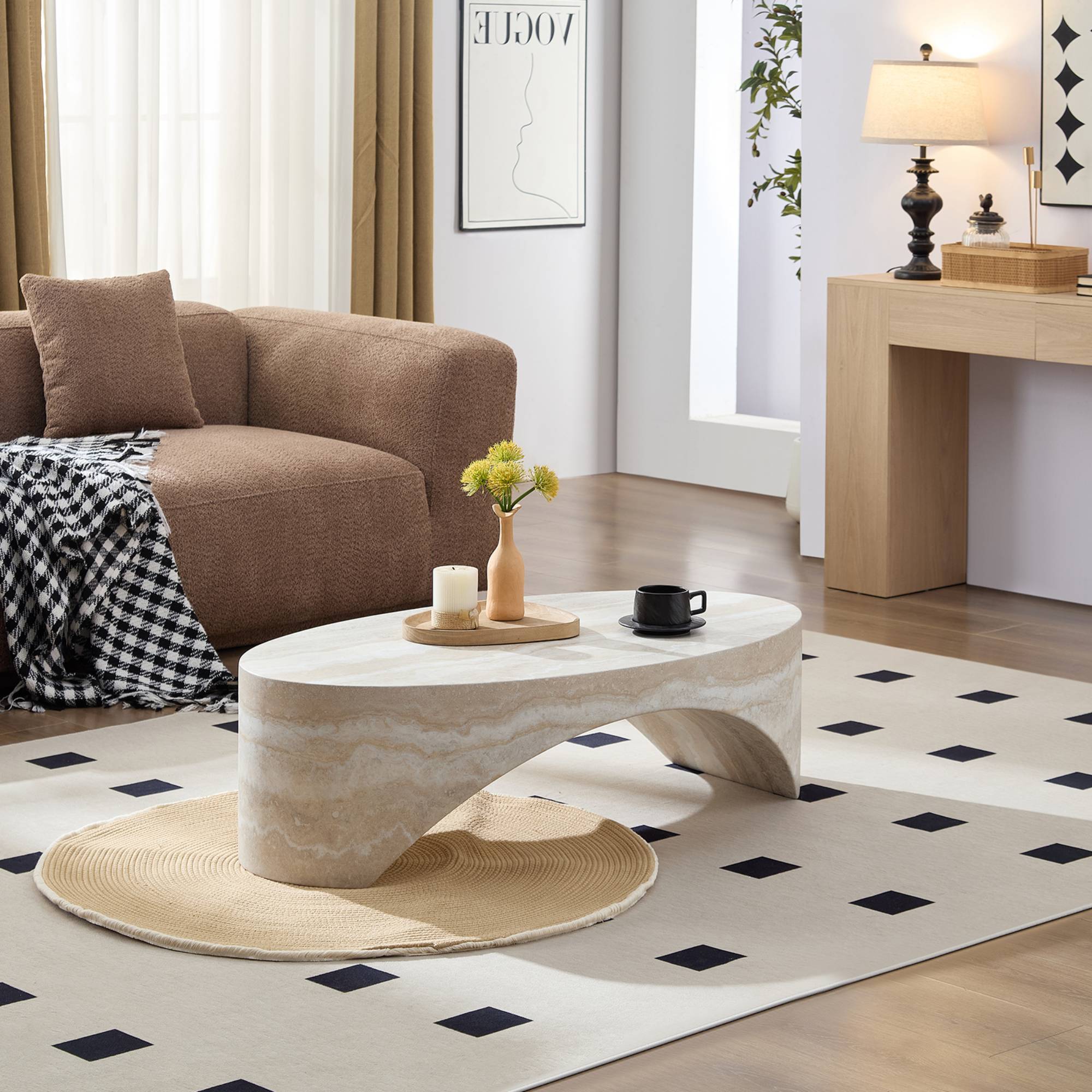 Modern oval marble coffee table with sculptural base, styled with candles and flowers in a cozy living room setting.
